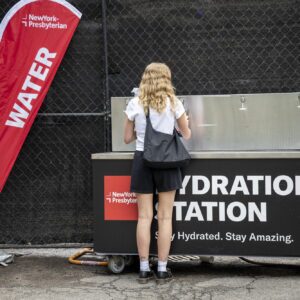 A person with blonde hair, white tee and black skirt, filling water at a water station